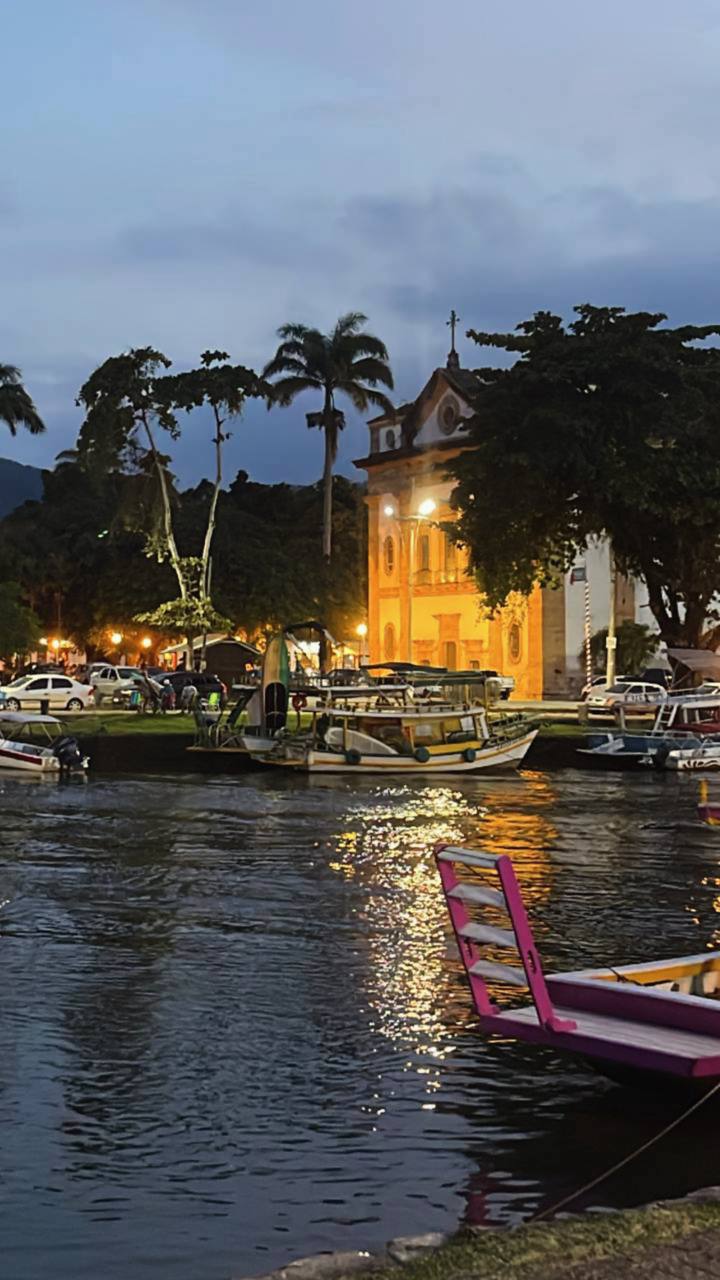 Vista noturna de rio com barcos coloridos e igreja iluminada ao fundo em Minas Gerais